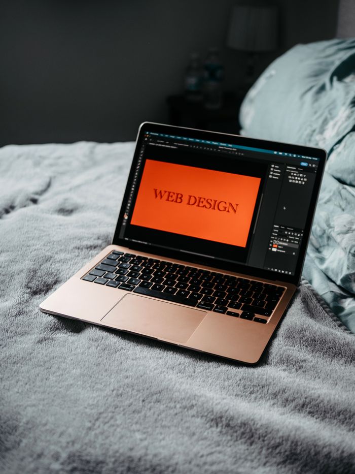 about-us-02 A laptop on a bed showing web design software, creating a cozy workspace.